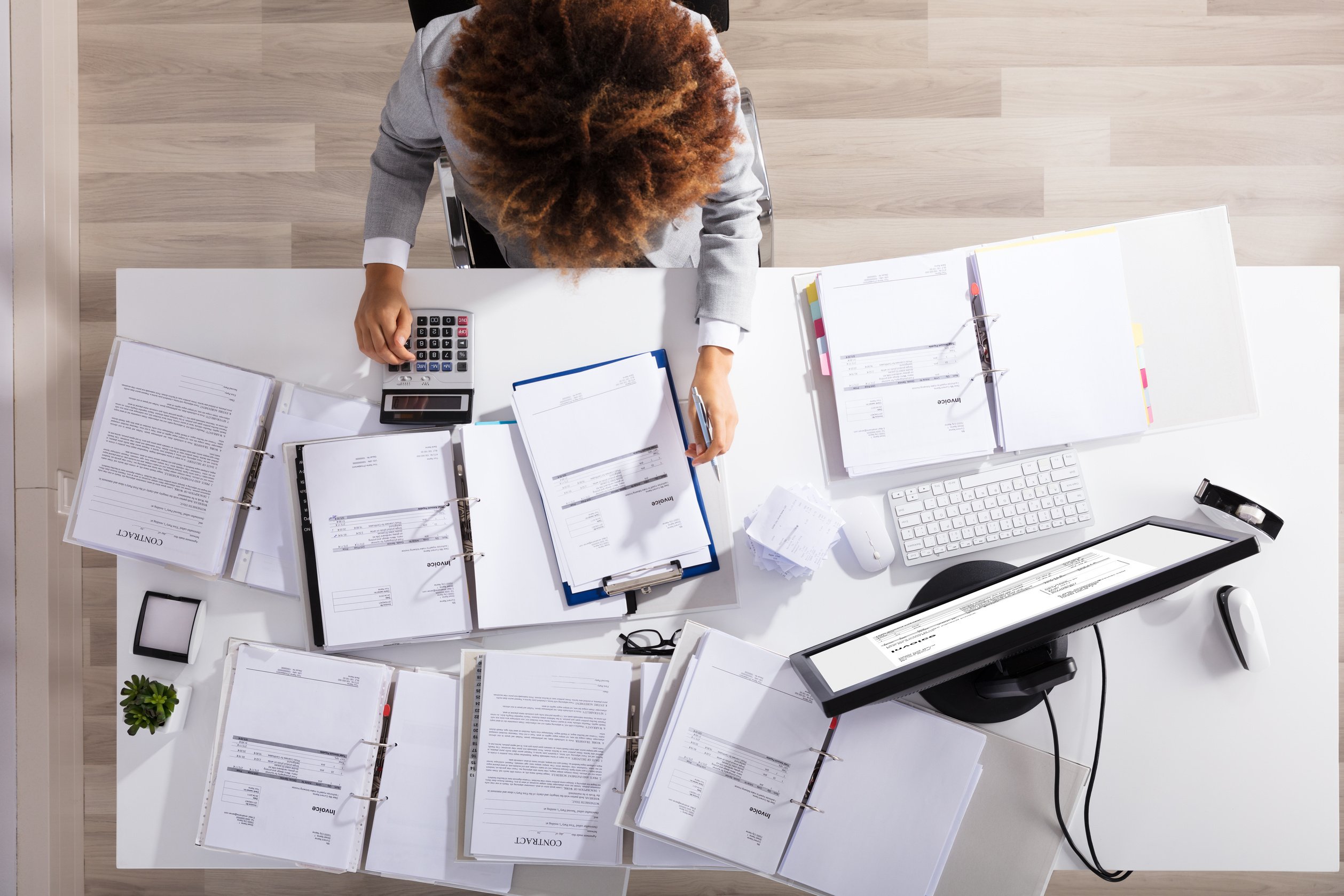 Accountant Surrounded by Documents Pressing on a Calculator 